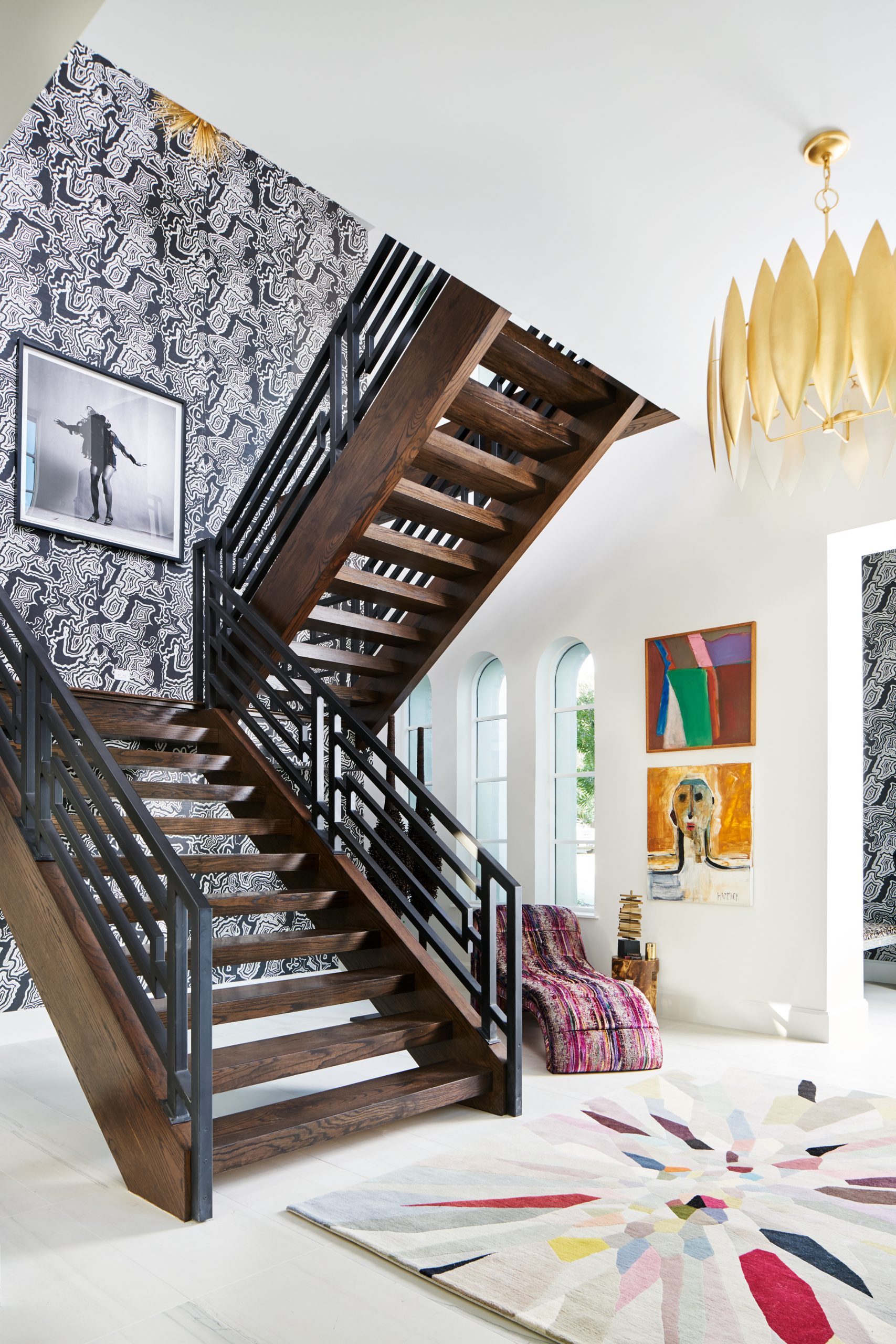 Traditional Home Dallas Showhouse, Bridget Beari Wallcovering, Buscemi wall covering, tina turner art, geometric railing, chaise lounger, s. harris brushstroke, double volume entry, modern staircase, entryway, circa lighting, gold chandelier, green and gold lamp, easel, Jonathan Adler easel, coffee table books, tom ford book, harpers bazaar book, credenza, dark credenza, black credenza, circle accent furniture, bowl, s. harris, drapery, curtains , gold lighting, gold chandelier, colorful rug, the rug company, original art, human form art