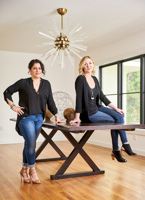 Two luxury interior designers sitting on a dining table with brass starburst chandelier at Pulp Design Studios