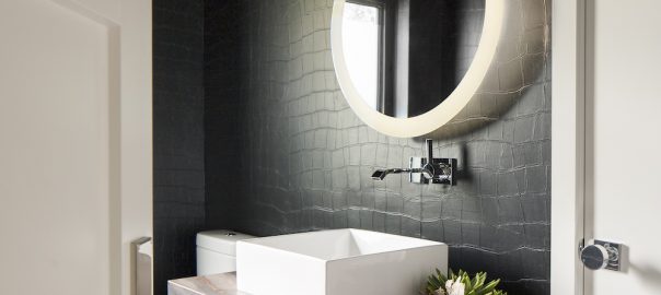 Contemporary powder bathroom interior design with circular mirror, crocodile inspired dark wallcovering and modern fixtures.